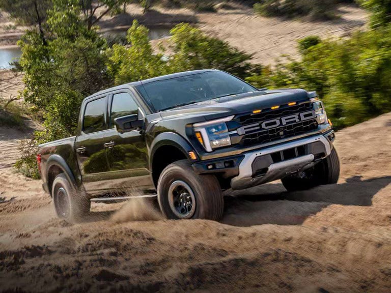 a dark f-150 raptor driving on a dirt path
