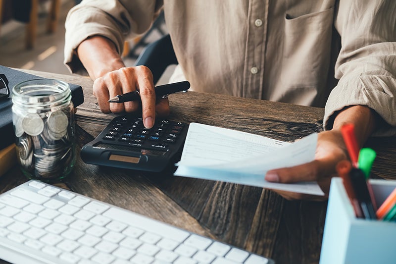 a person sitting at a desk with a calculator, paper, and pen.